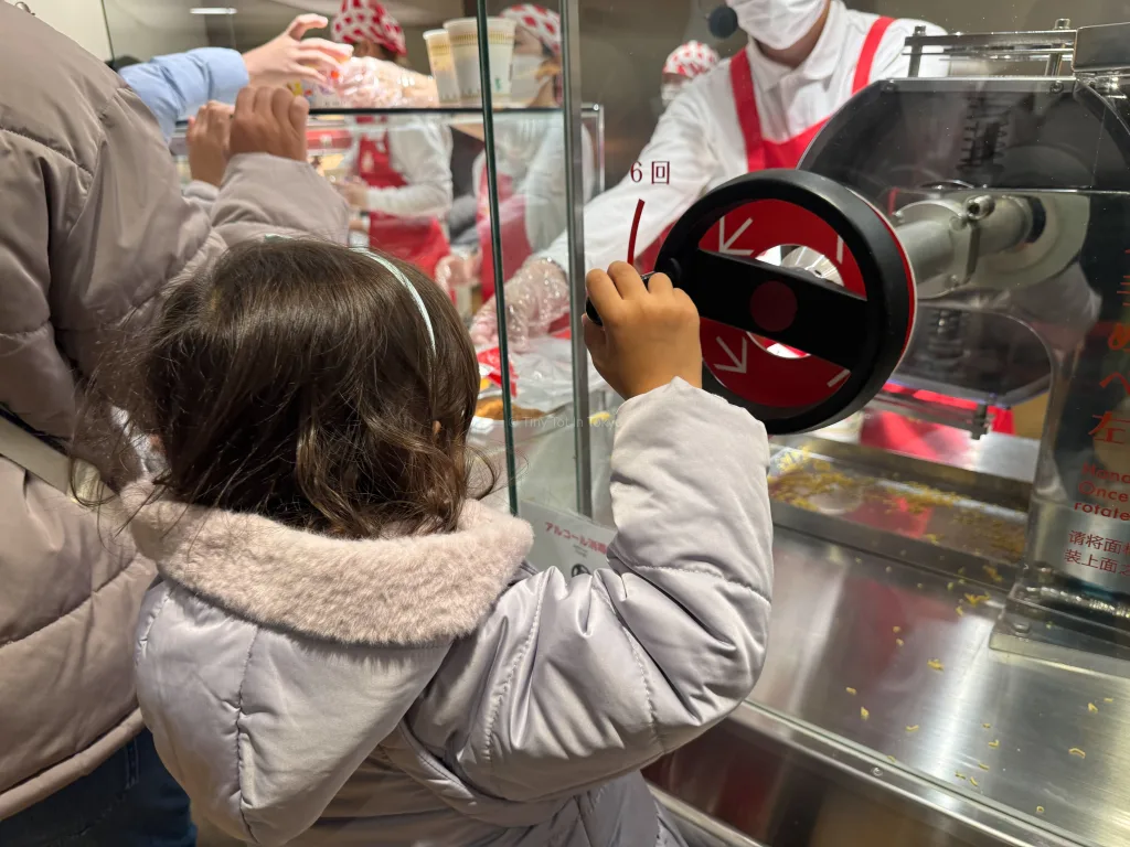 My daughter turning a lever to put ramen into her cup noodles container at the cup noodle factory