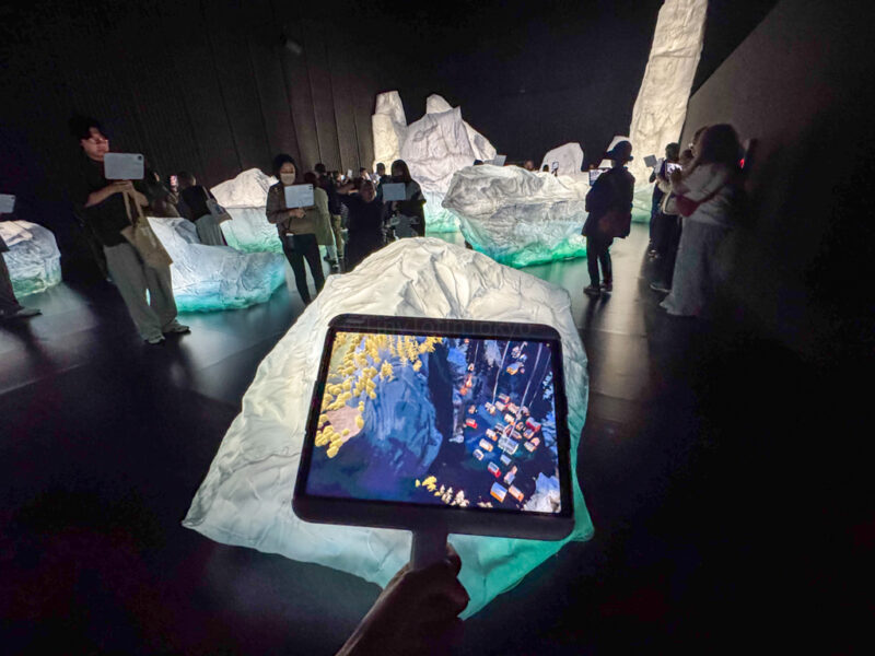 A girl holding a screen towards fake icebergs at the Osaka Expo Canada Pavilion AR Experience