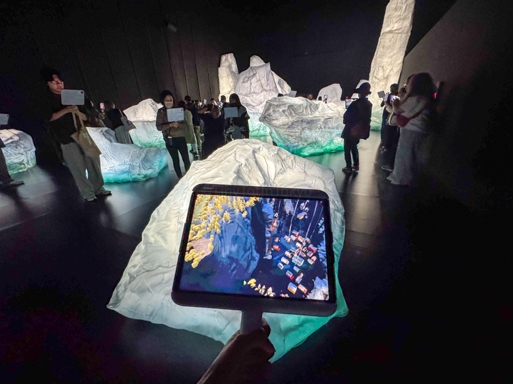 A girl holding a screen towards fake icebergs at the Osaka Expo Canada Pavilion AR Experience