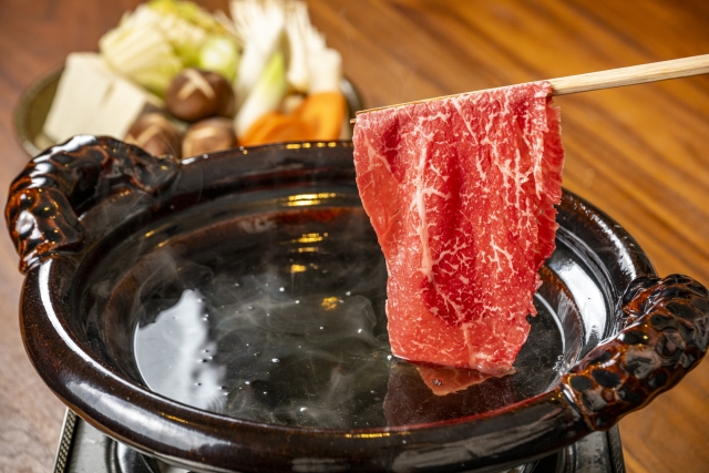 a piece of meat being held above a pot of broth for shabu shabu