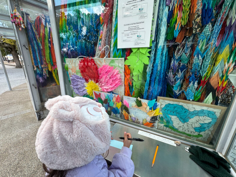 a child standing in front of paper cranes displayed in Hiroshima
