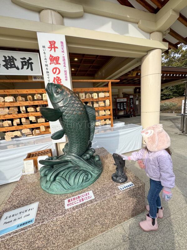 a girl standing next to a statue of a fish at gokoku shrine in hiroshima