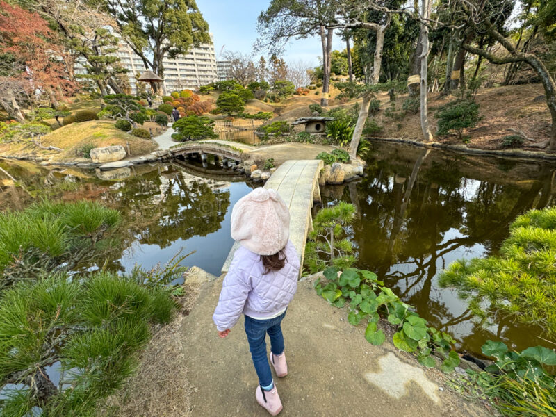 a girl walking on a bridge over a pond at Shukkeien Garden in Hiroshima
