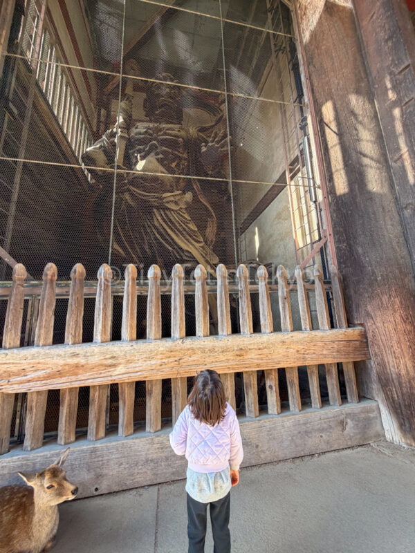 a deer and a child looking at a statue at the gate of Todaiji
