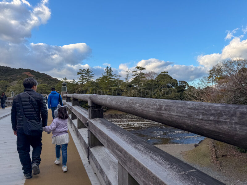 a parent and child walking on a bridge at ise jingu naiku