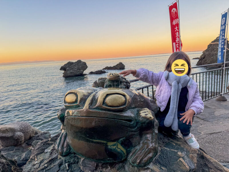 a child standing next to a frog statue at Futami Okitama Shrine